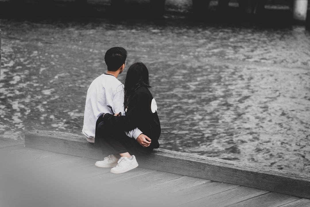 a man and a woman sitting on a dock looking at the water,