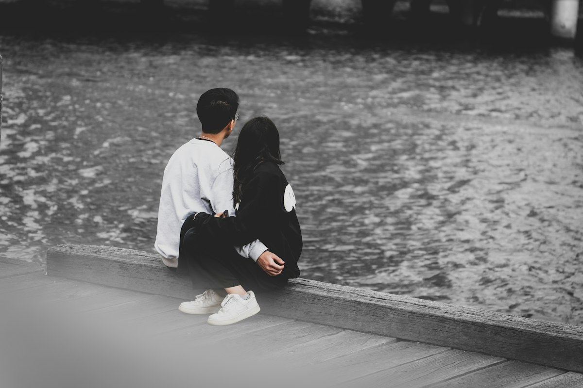 a man and a woman sitting on a dock looking at the water