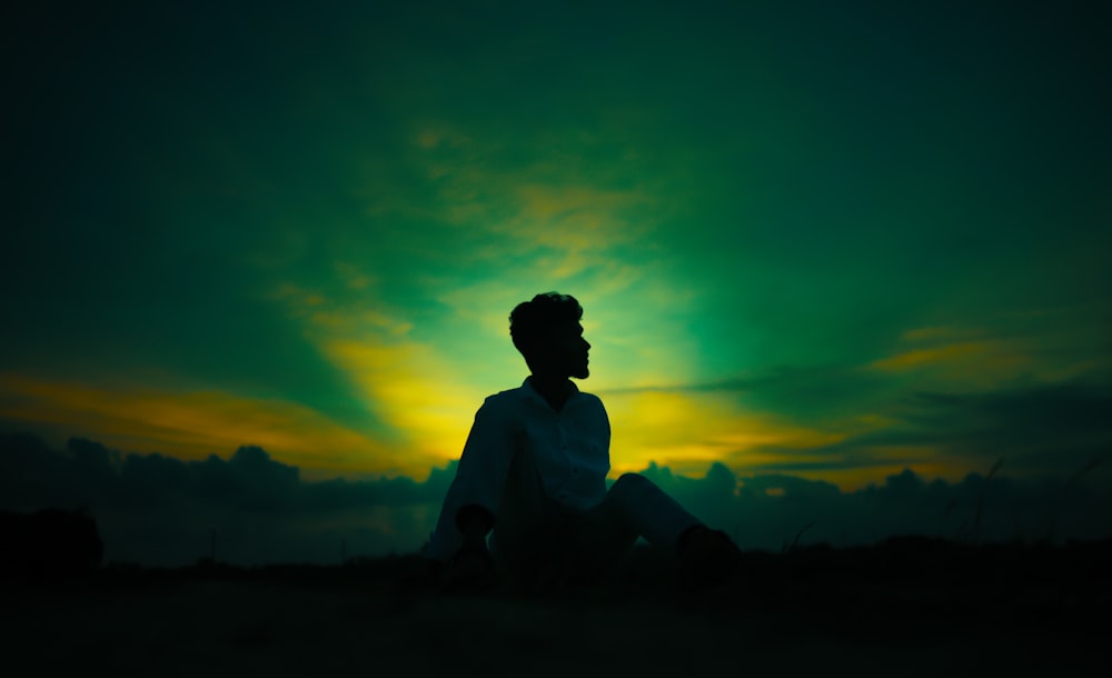 a man sitting on the ground in front of a sunset