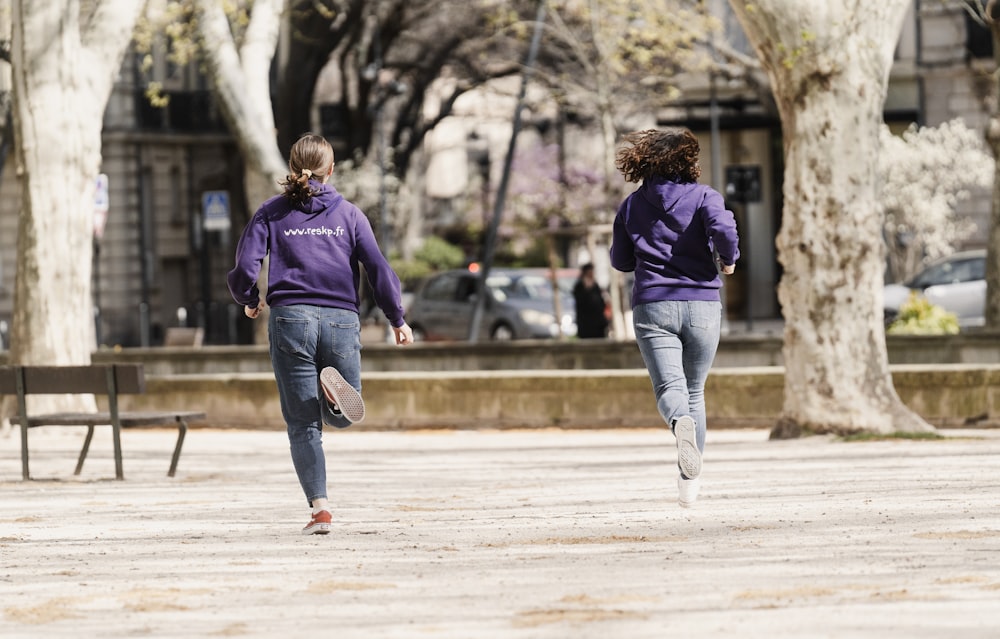two women in purple jackets are running in a park