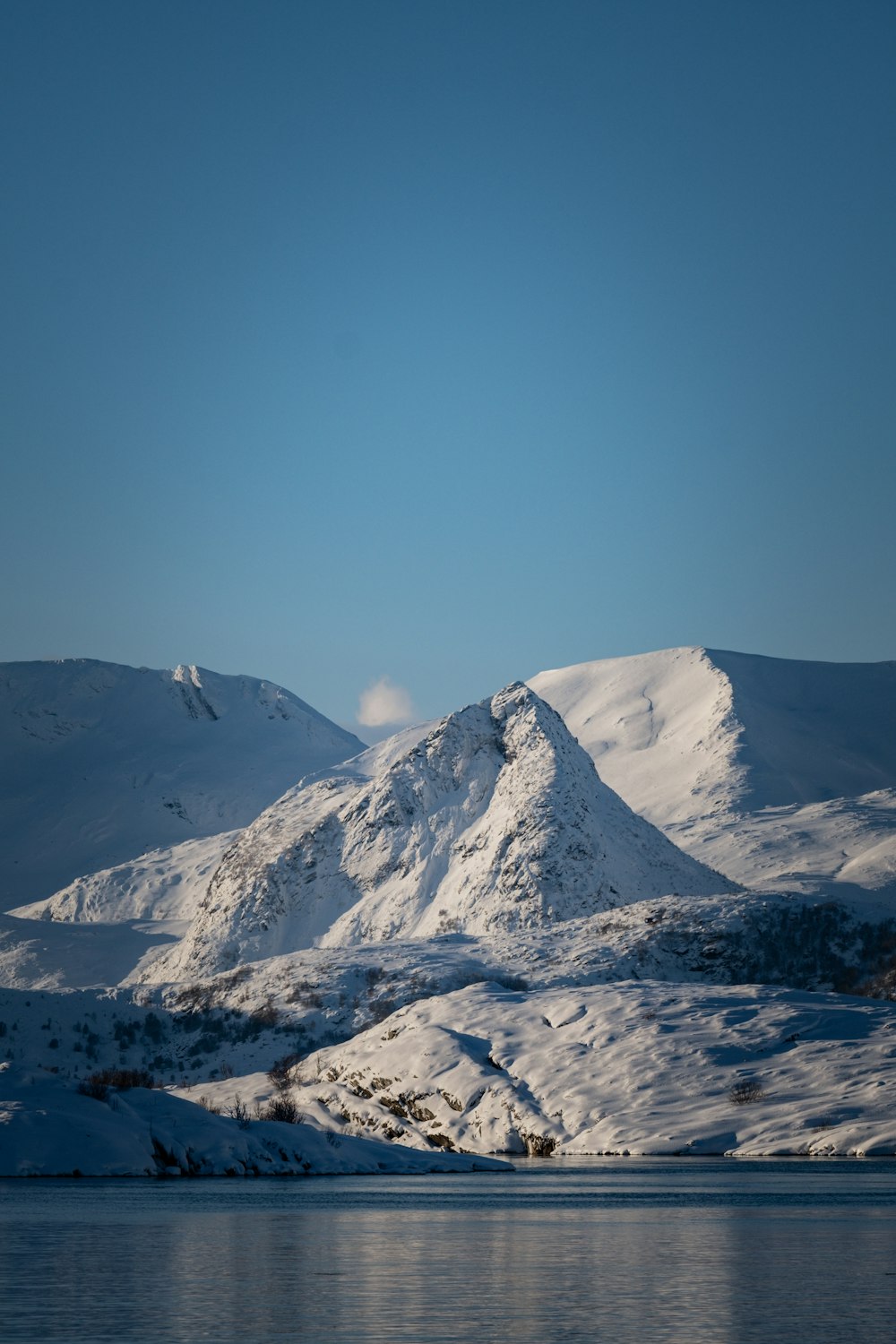 a mountain covered in snow next to a body of water