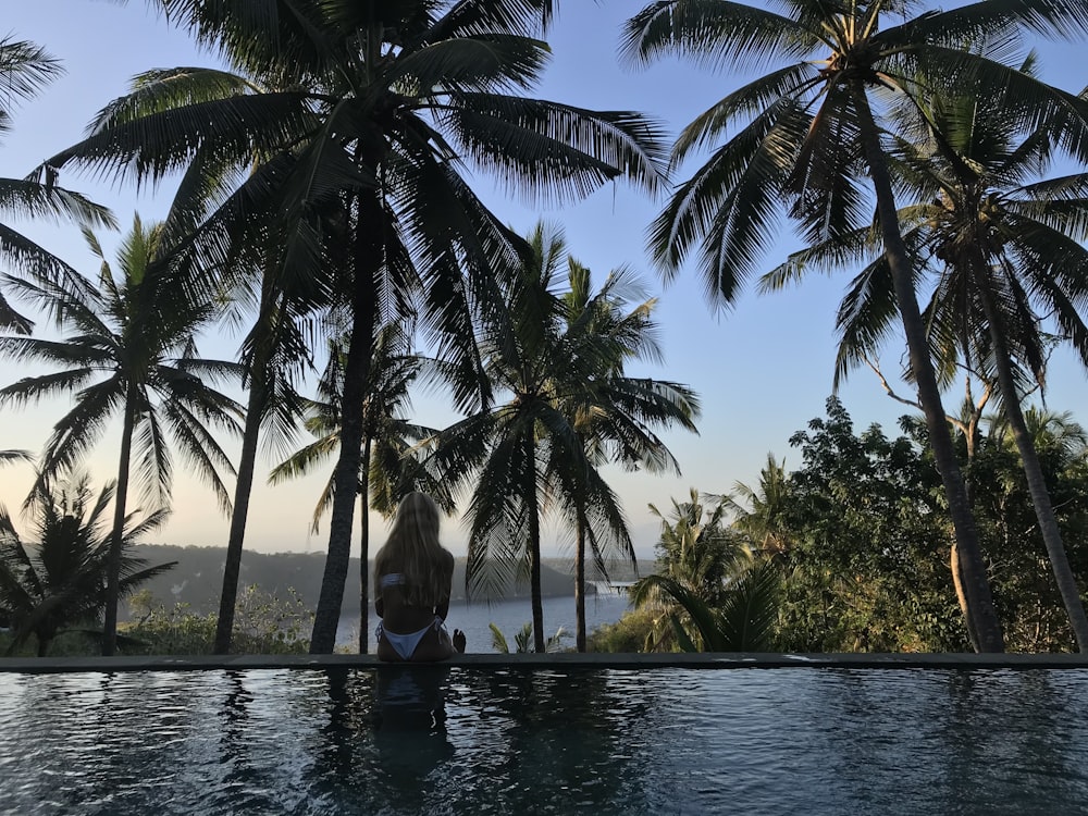 a woman sitting in a pool surrounded by palm trees