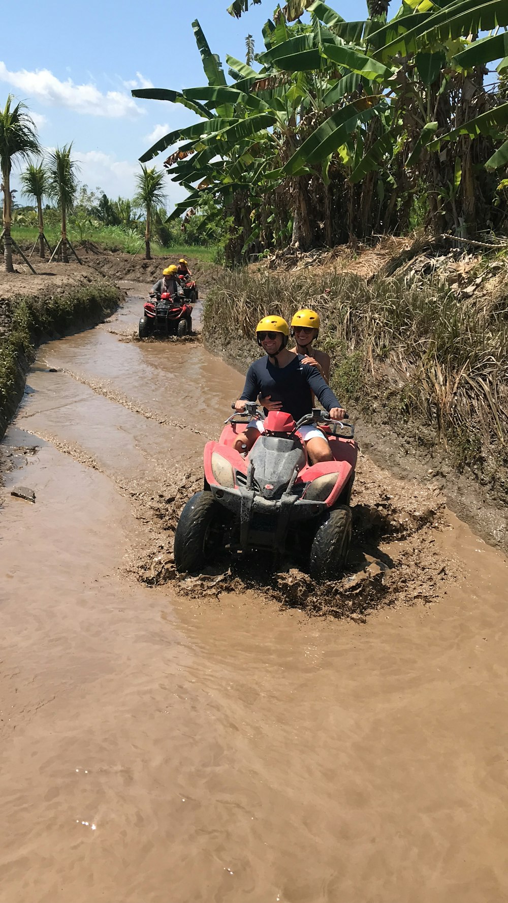 two people riding four wheelers through a muddy river