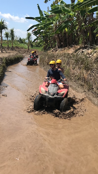 two people riding four wheelers through a muddy river