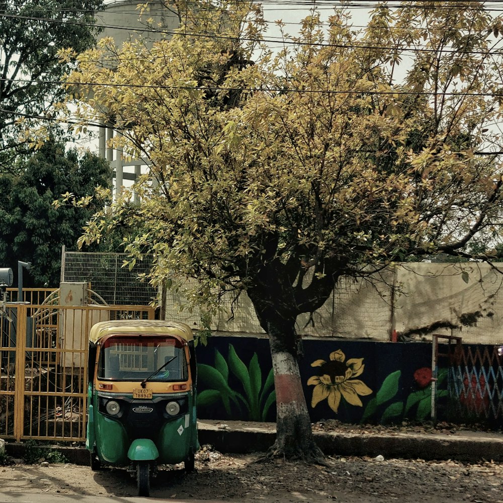 a small green and yellow vehicle parked next to a tree