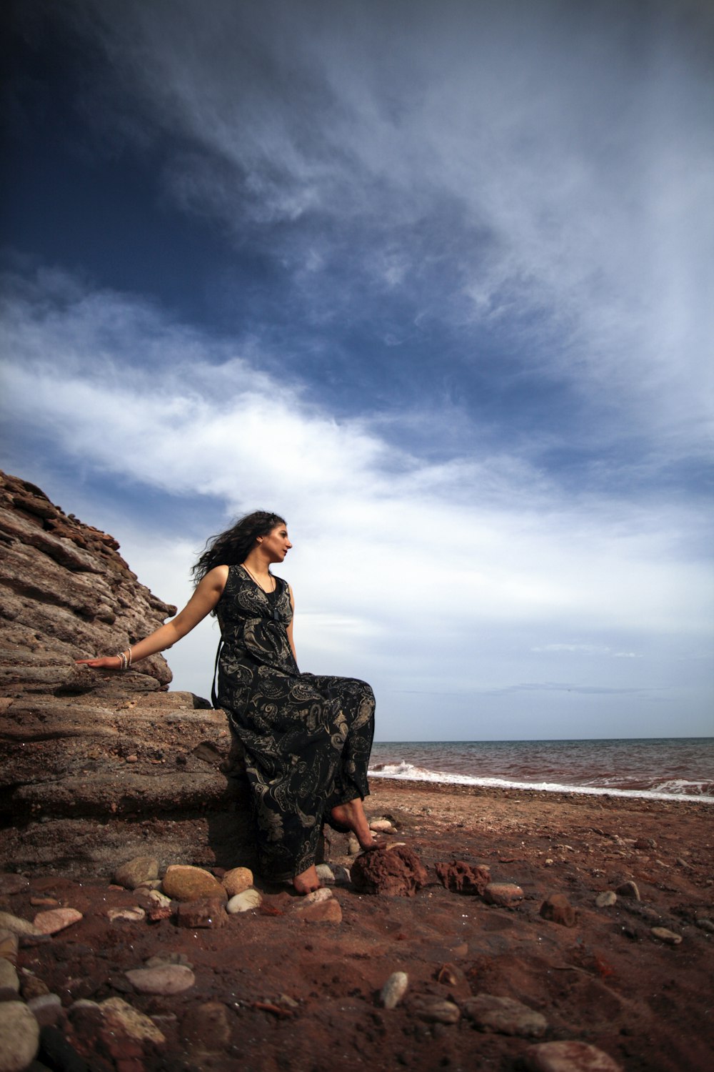 a woman sitting on a rock near the ocean