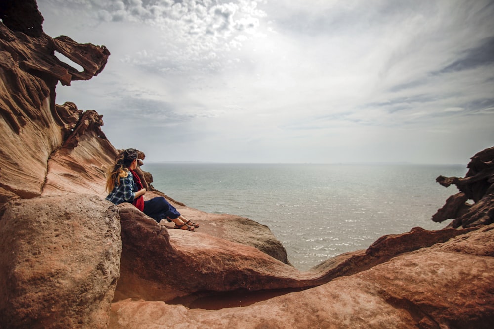 a couple of people sitting on top of a large rock