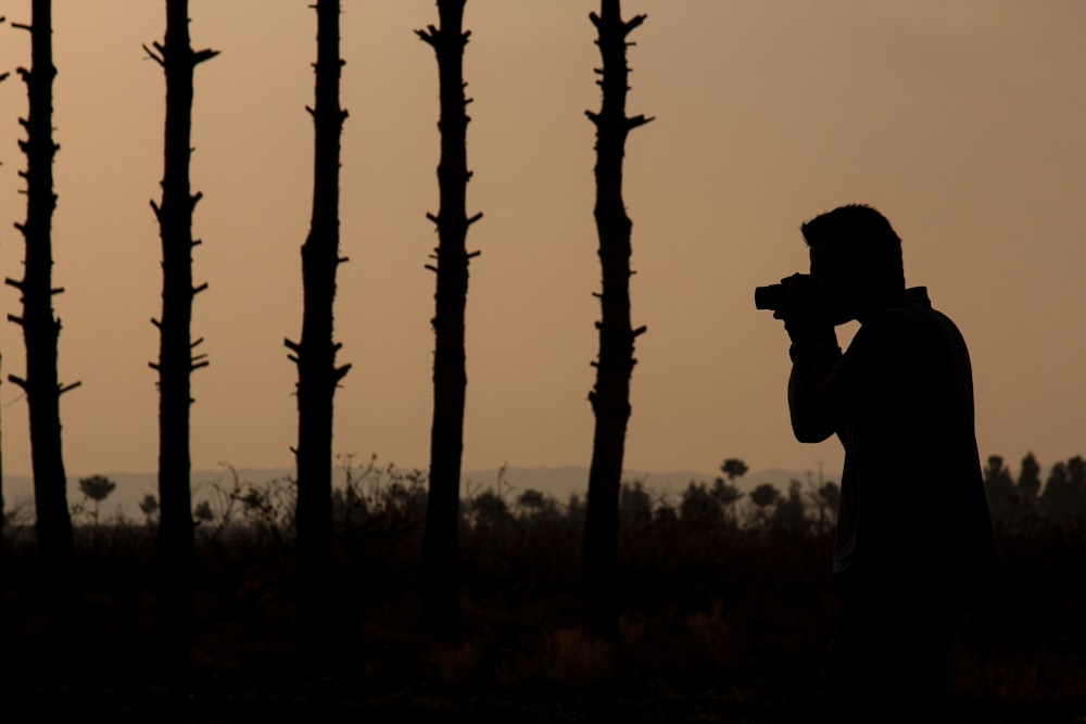 a man holding a camera in front of a line of trees