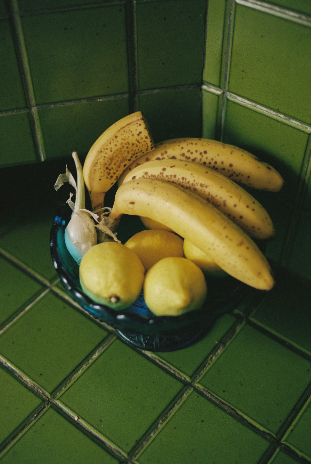 a bowl filled with bananas and lemons on a green tile floor