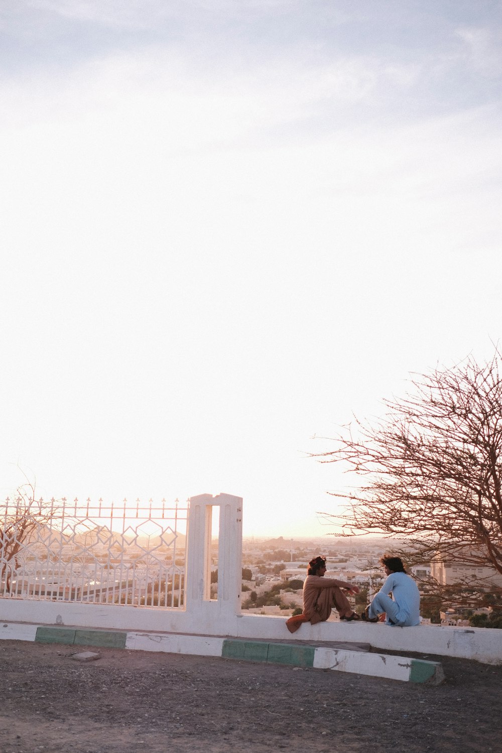 a couple of people sitting on top of a white fence