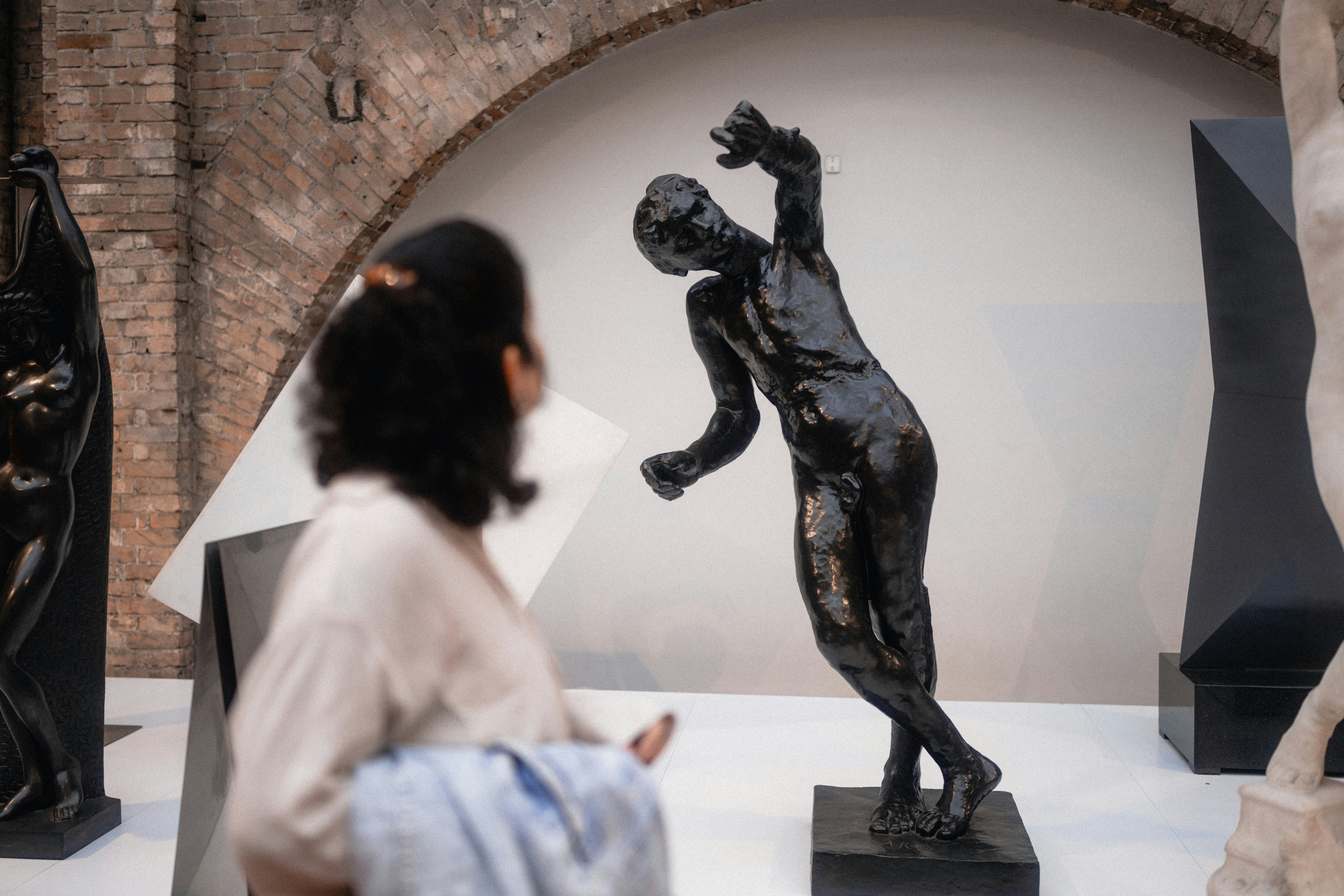 a museum visitor looks at a bronze statue of a leaning human figure
