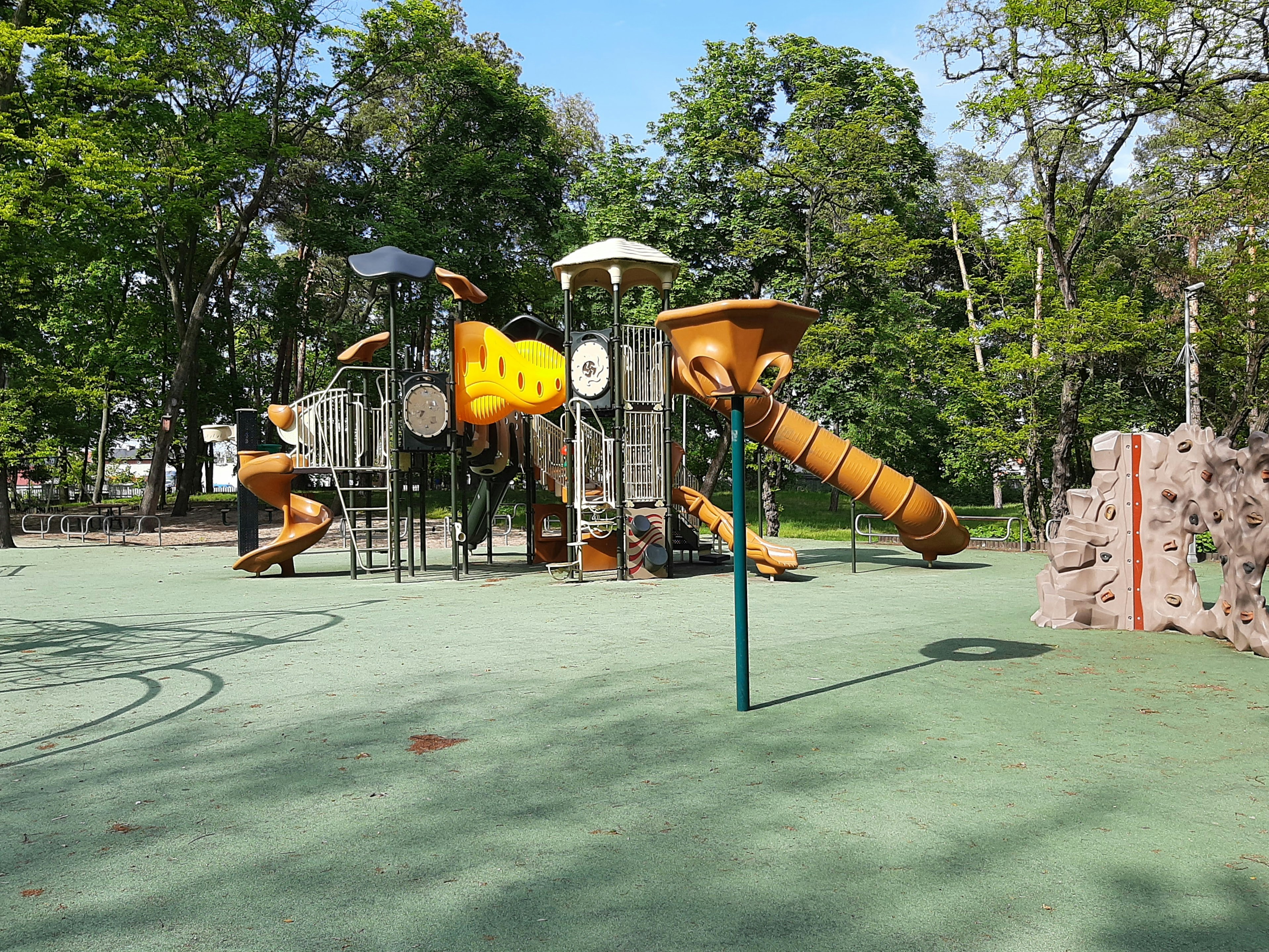Colorful outdoor playground with climbing structures, slides, and shaded areas surrounded by trees