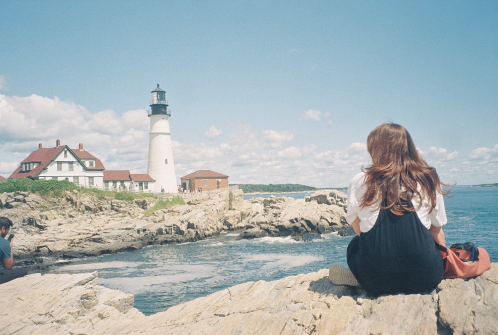 a woman sitting on a rock next to a body of water