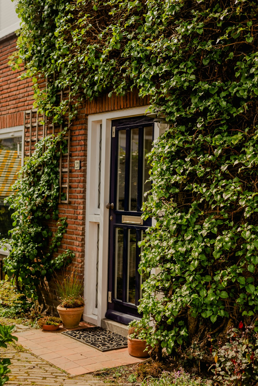 a brick building with a white door surrounded by greenery