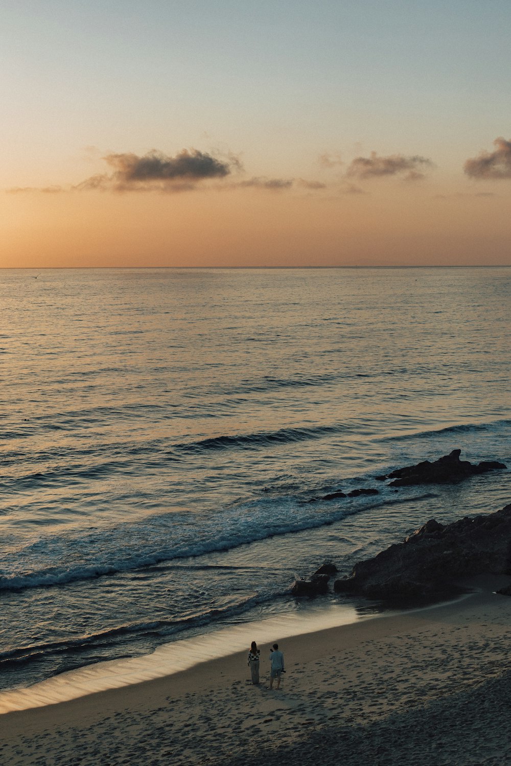 two people walking on the beach at sunset