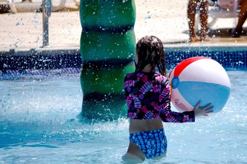 a little girl playing with a beach ball in a pool