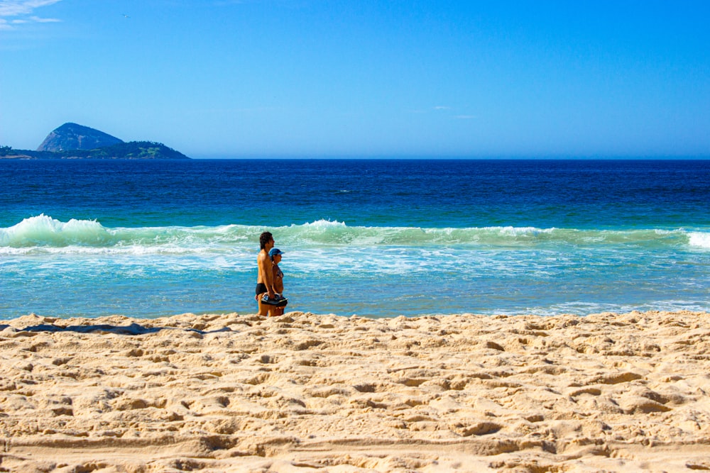 a man standing on top of a sandy beach next to the ocean