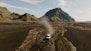 a truck driving down a dirt road in front of a mountain
