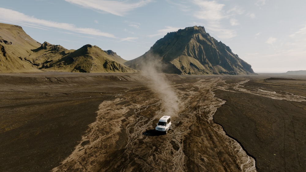 a truck driving down a dirt road in front of a mountain
