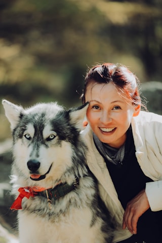 a woman sitting next to a husky dog