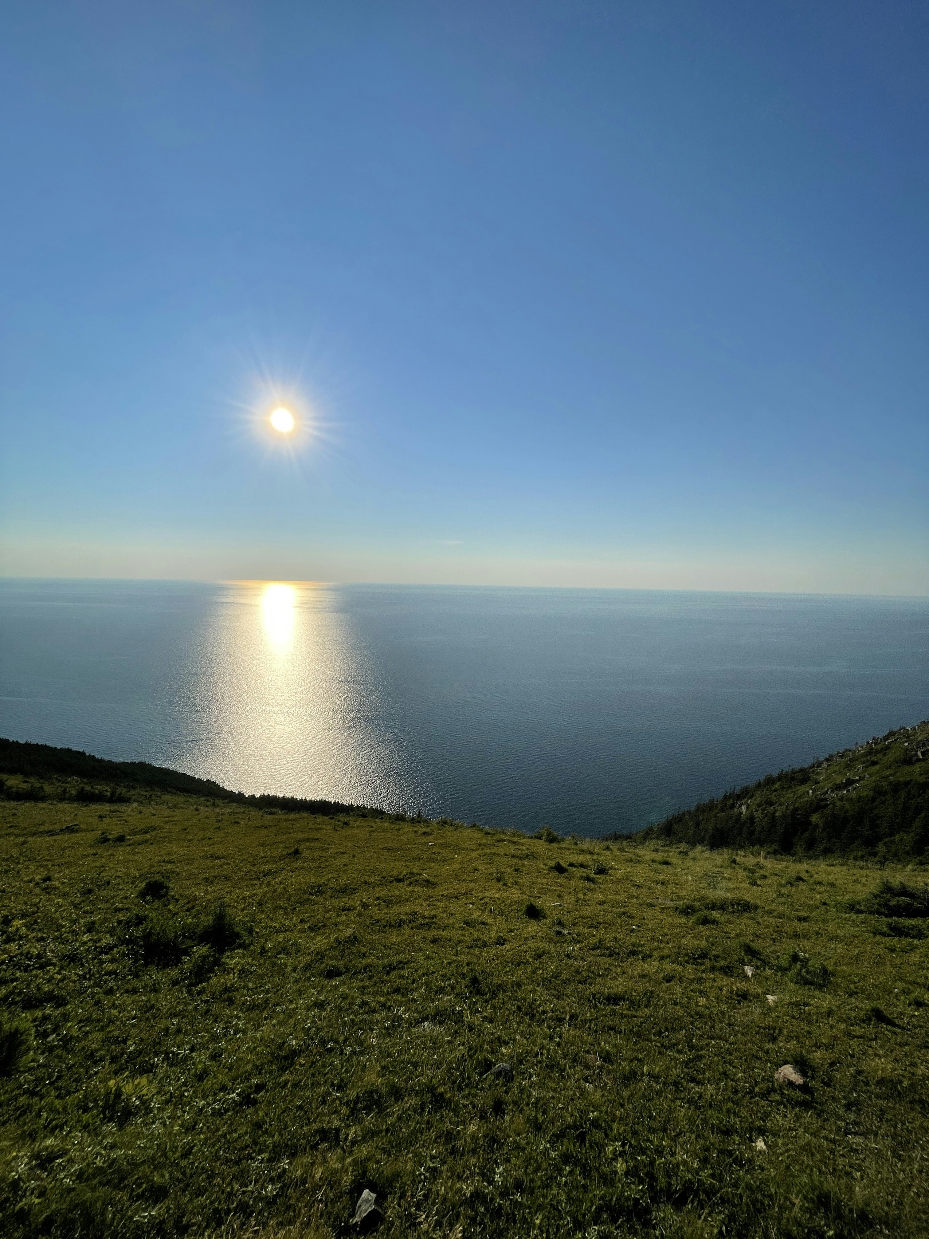 the sun is shining over the ocean on a hill