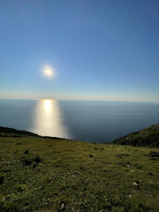 the sun is shining over the ocean on a hill