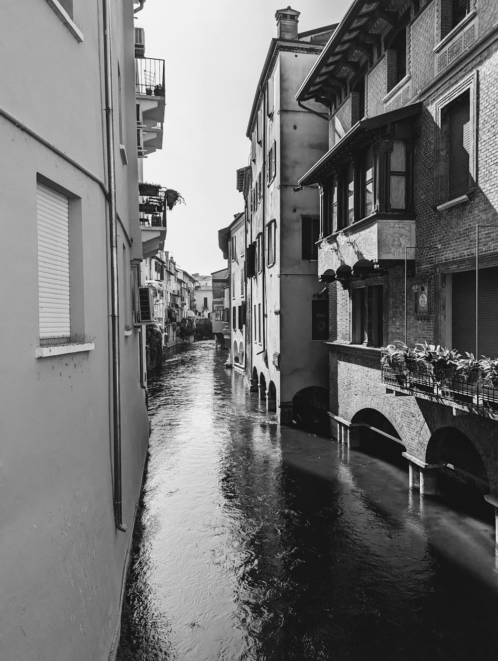 a black and white photo of a canal in a city