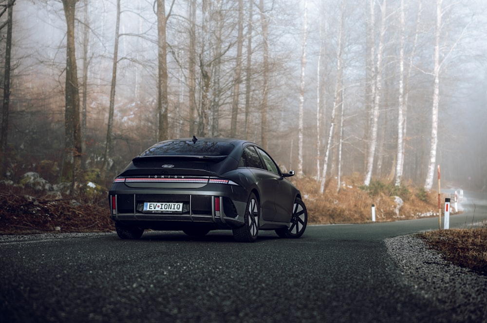 a black sports car driving down a road in the woods
