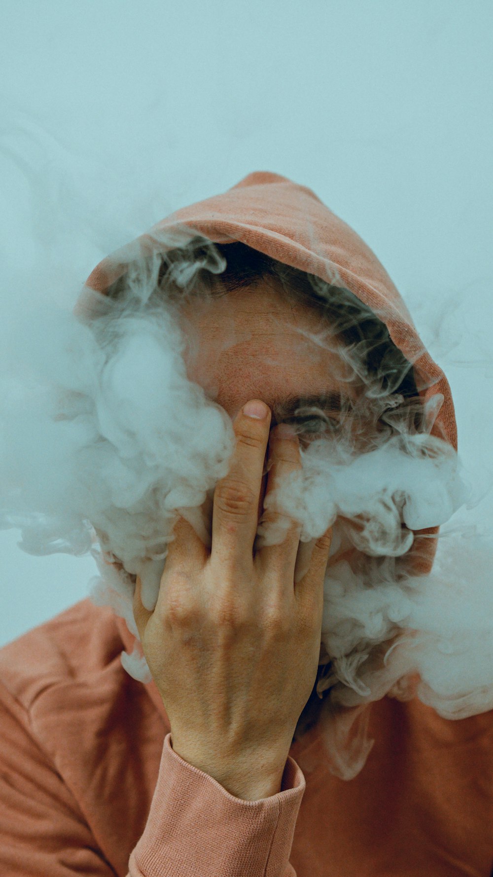 a person with a hoodie is smoking a cloud of smoke