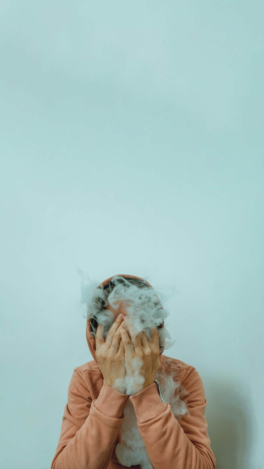 uma pessoa cobrindo o rosto com uma nuvem de fumaça
