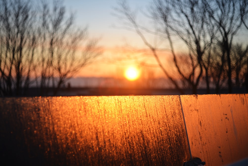 the sun is setting over the water behind a fence