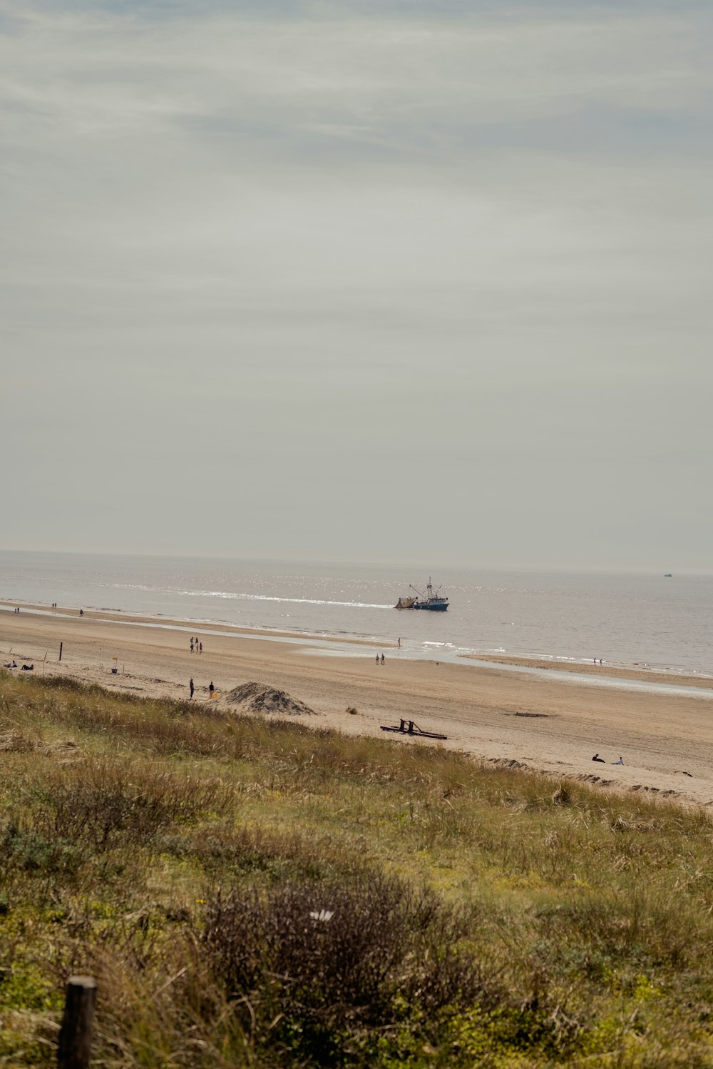 a beach with people walking on it and a boat in the water