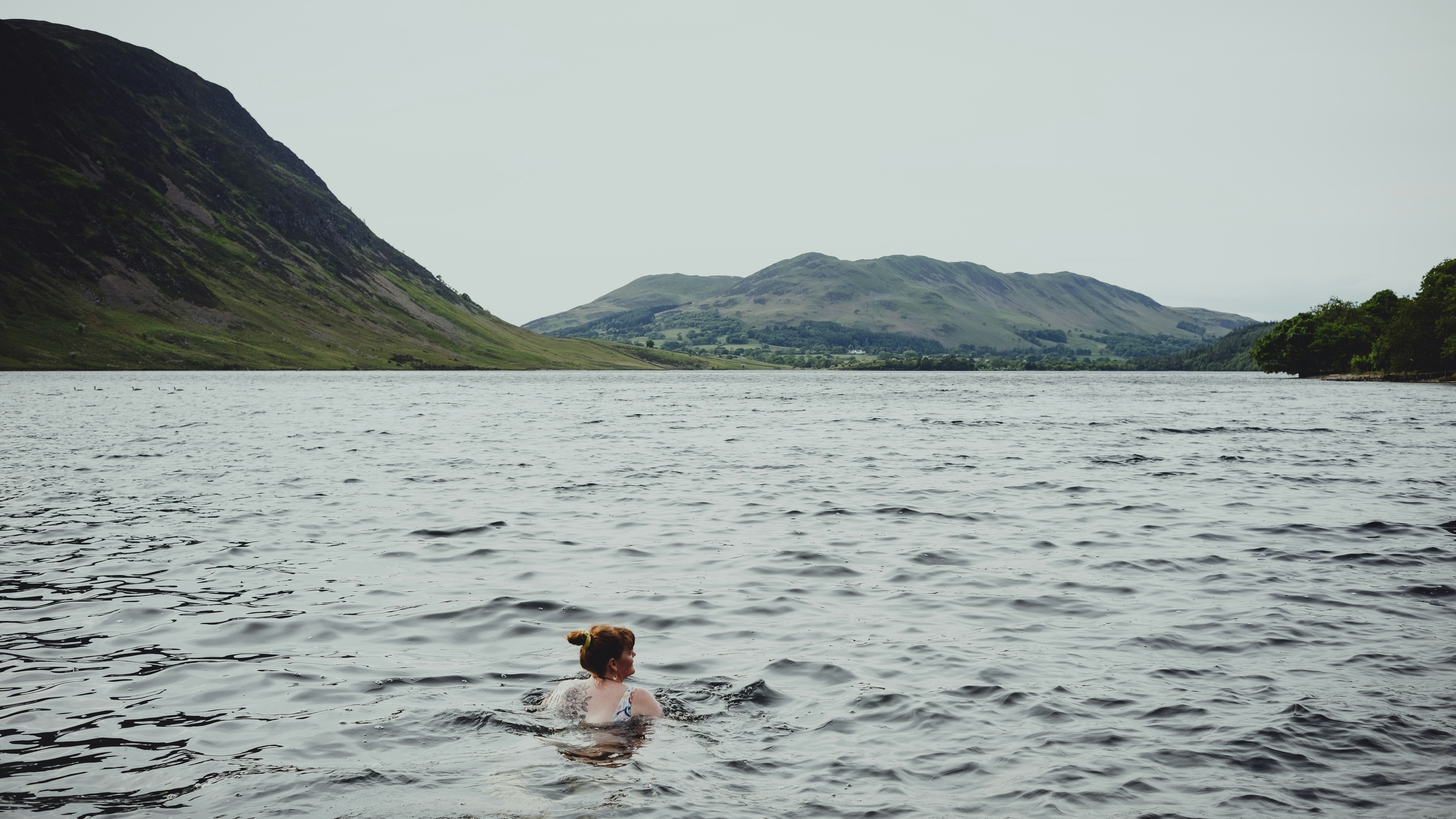 a woman swimming in a lake with mountains in the background