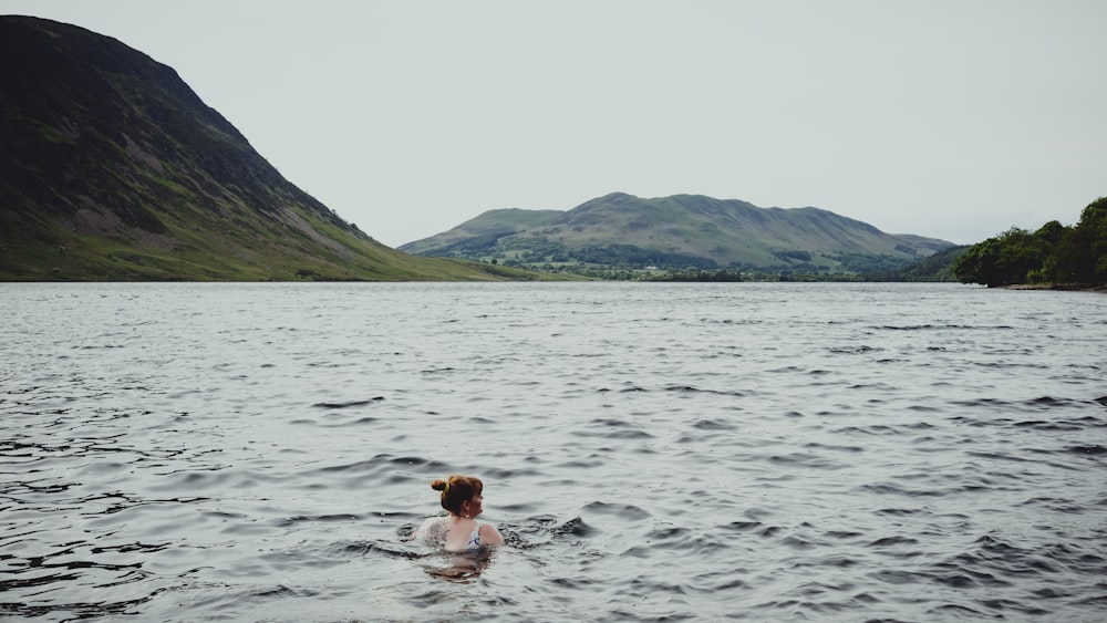 a woman swimming in a lake with mountains in the background