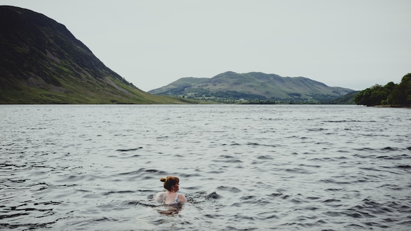 Wild swimmer in a cold lake with green hills in the background, UK lake district