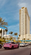 a pink car driving down a street next to tall buildings