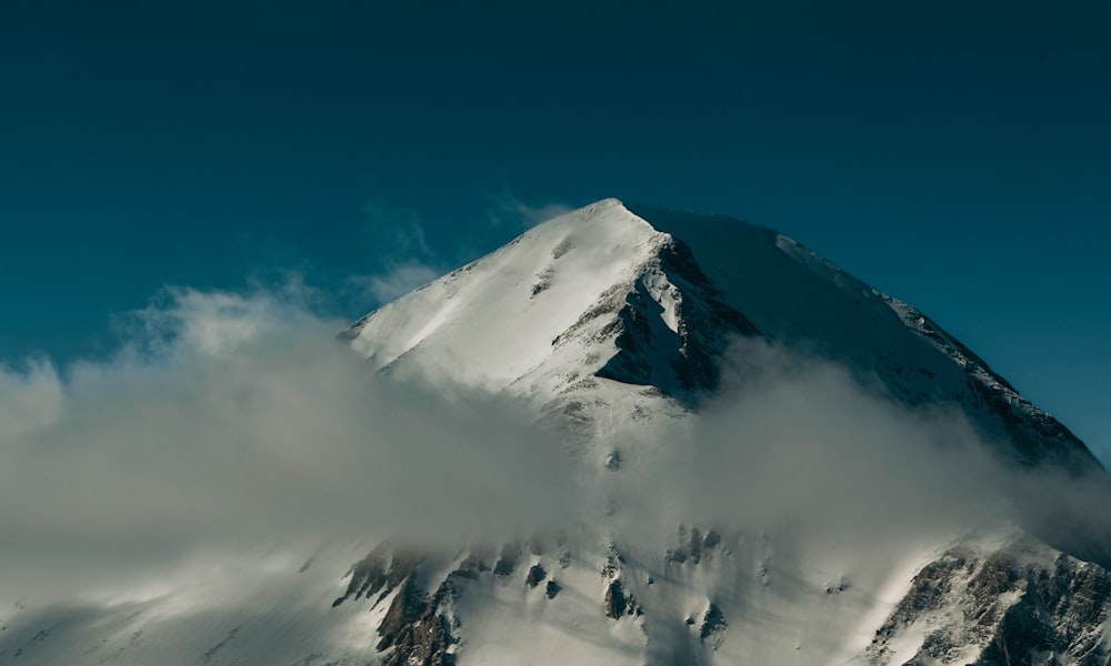 a mountain covered in snow and clouds under a blue sky