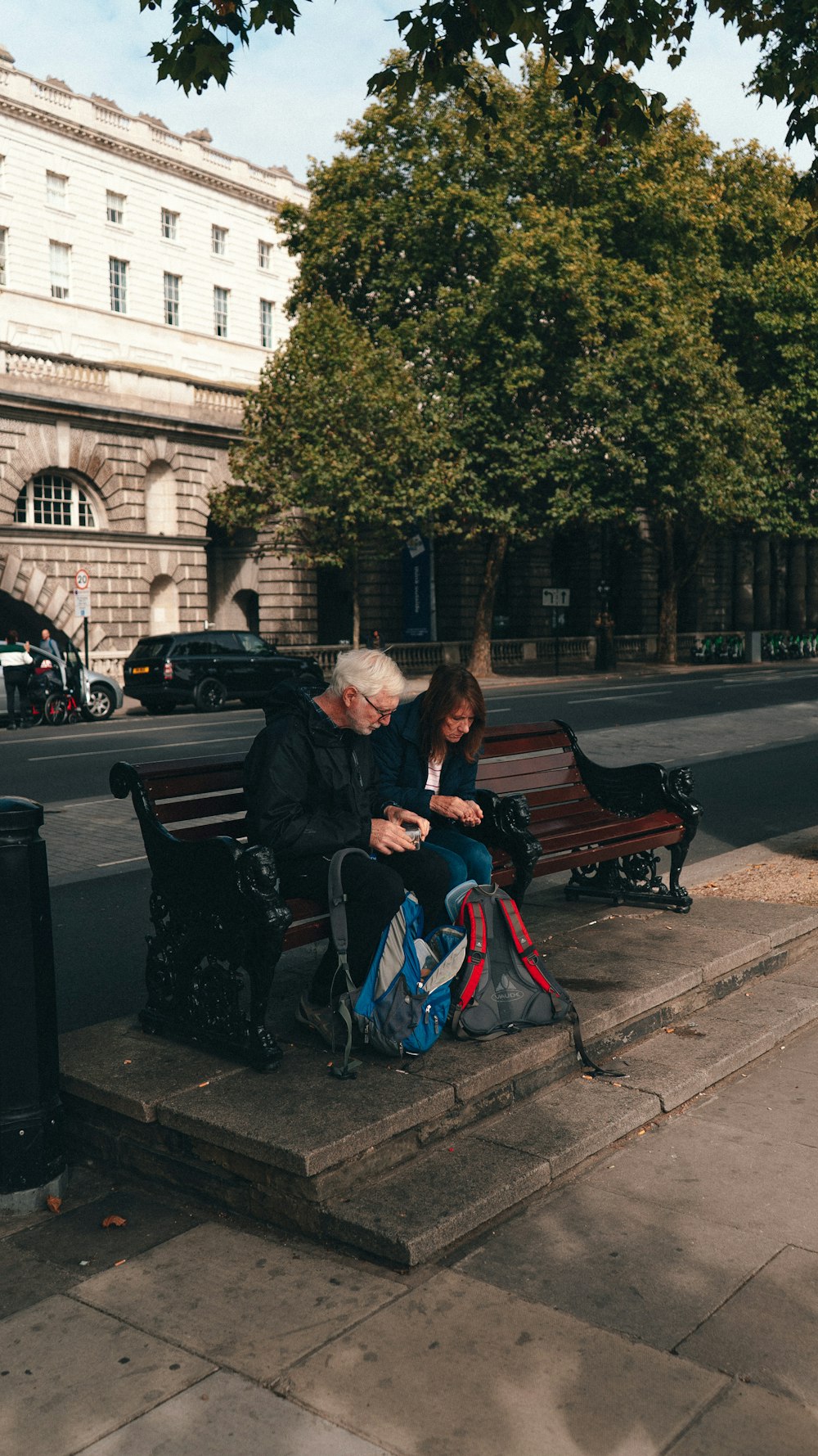 a man and woman sitting on a bench looking at a cell phone