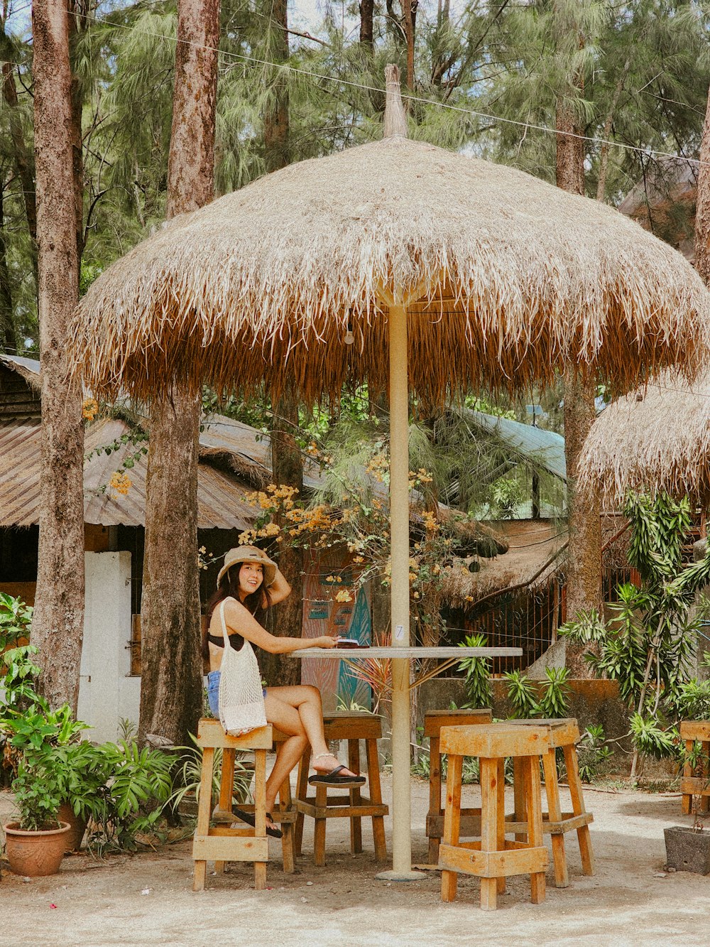 a woman sitting at a table under a straw umbrella