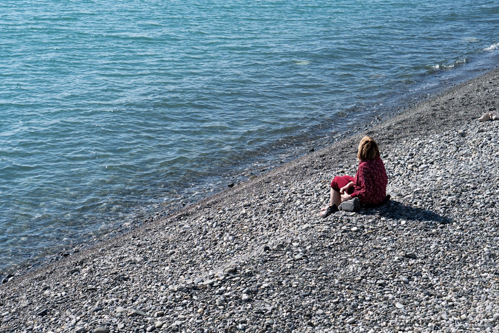 a little girl sitting on a beach next to a body of water