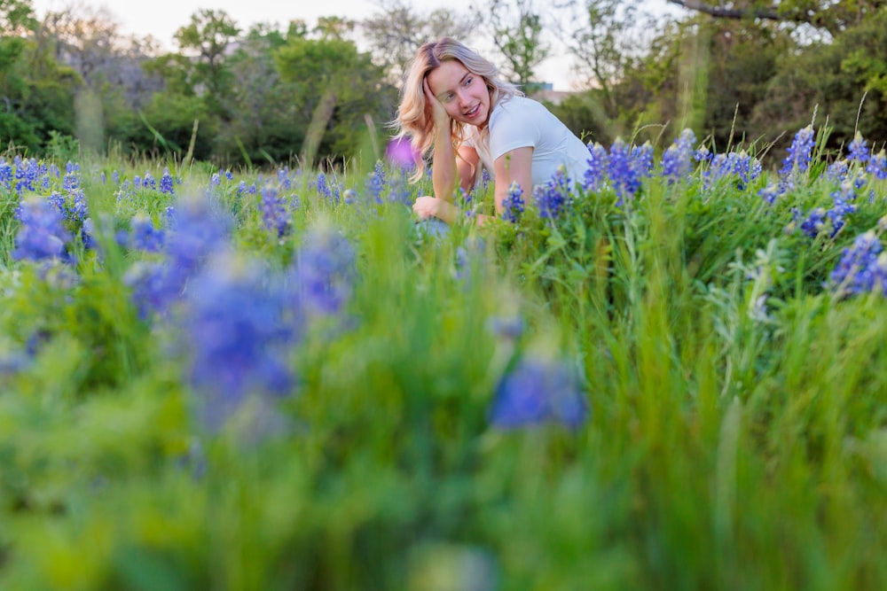 una donna inginocchiata in un campo di fiori blu
