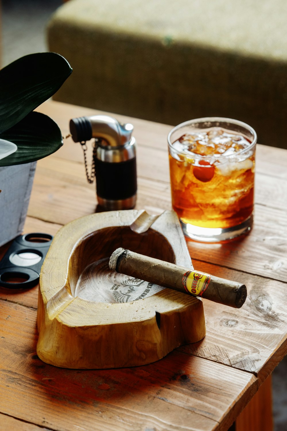 a wooden table topped with a glass of alcohol and a cigar