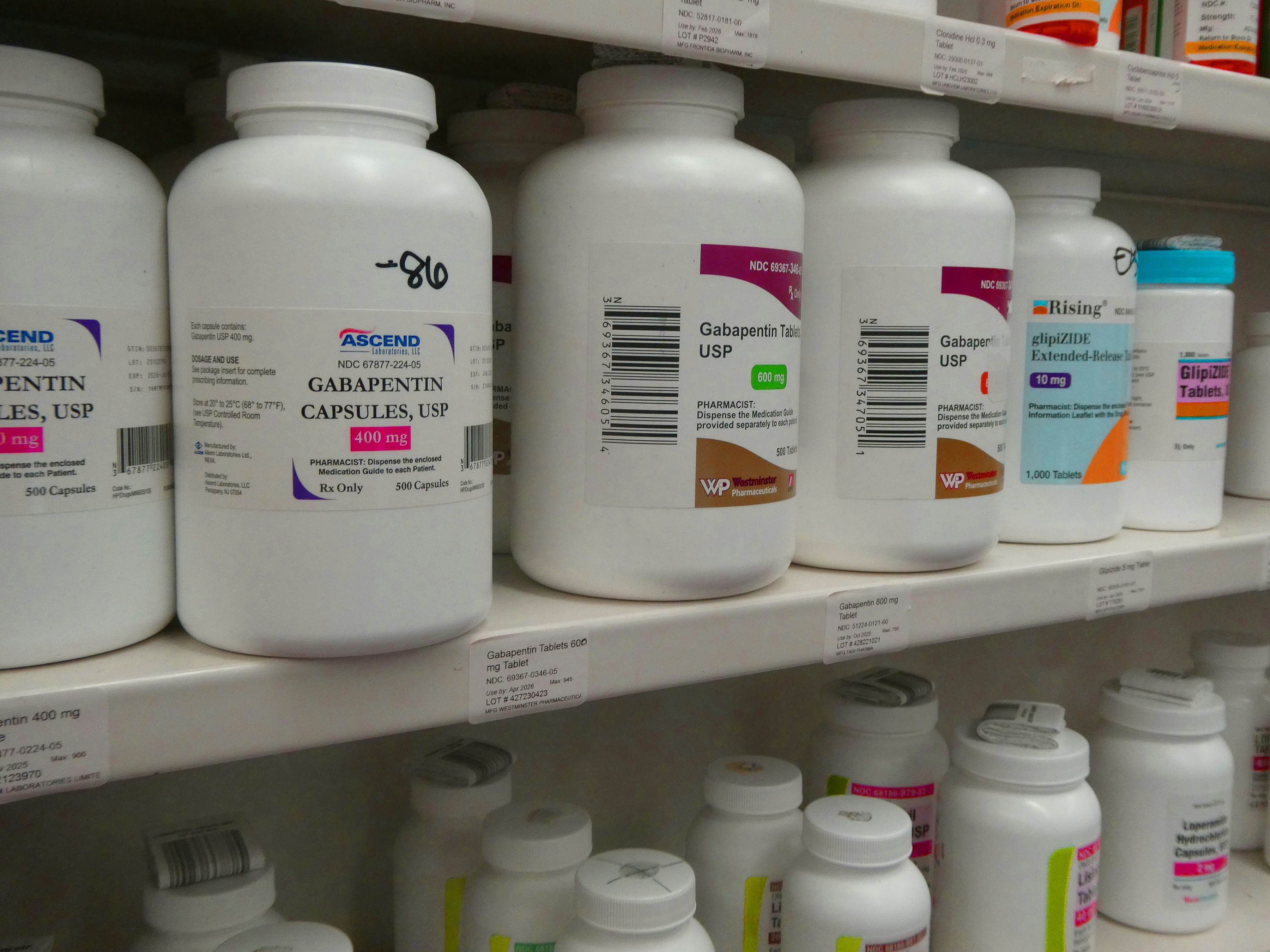 Rows of medicine bottles and blister packs neatly arranged on bright white pharmacy shelves
