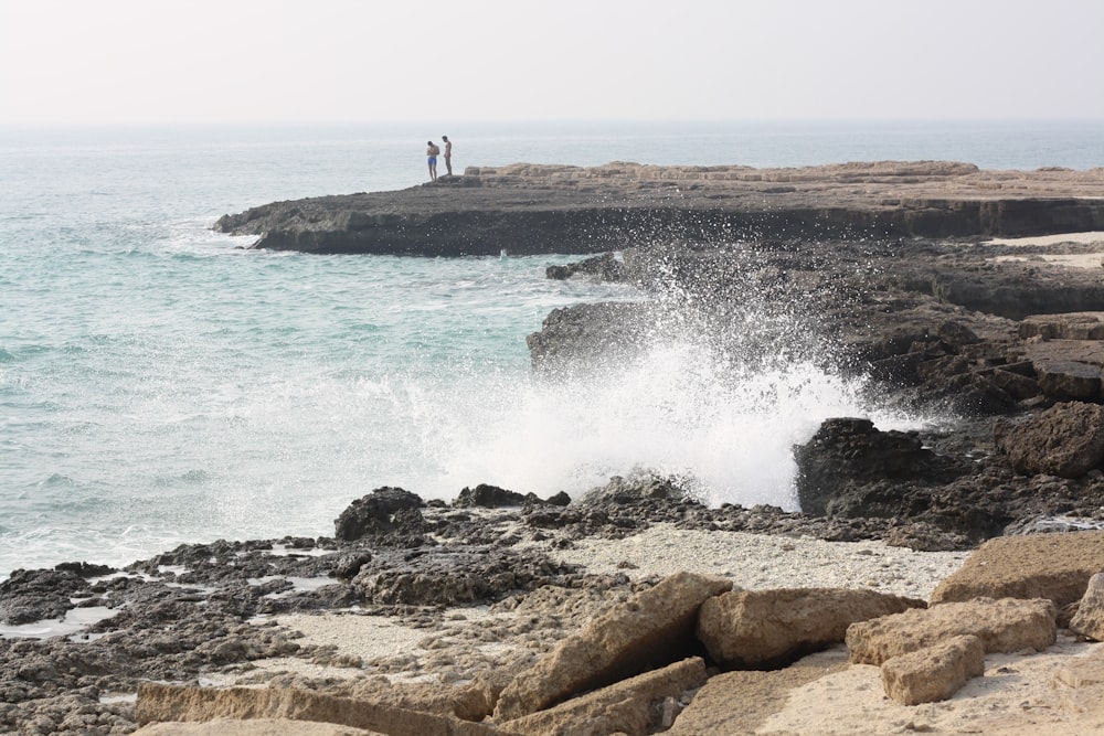 a couple of people standing on top of a rocky beach