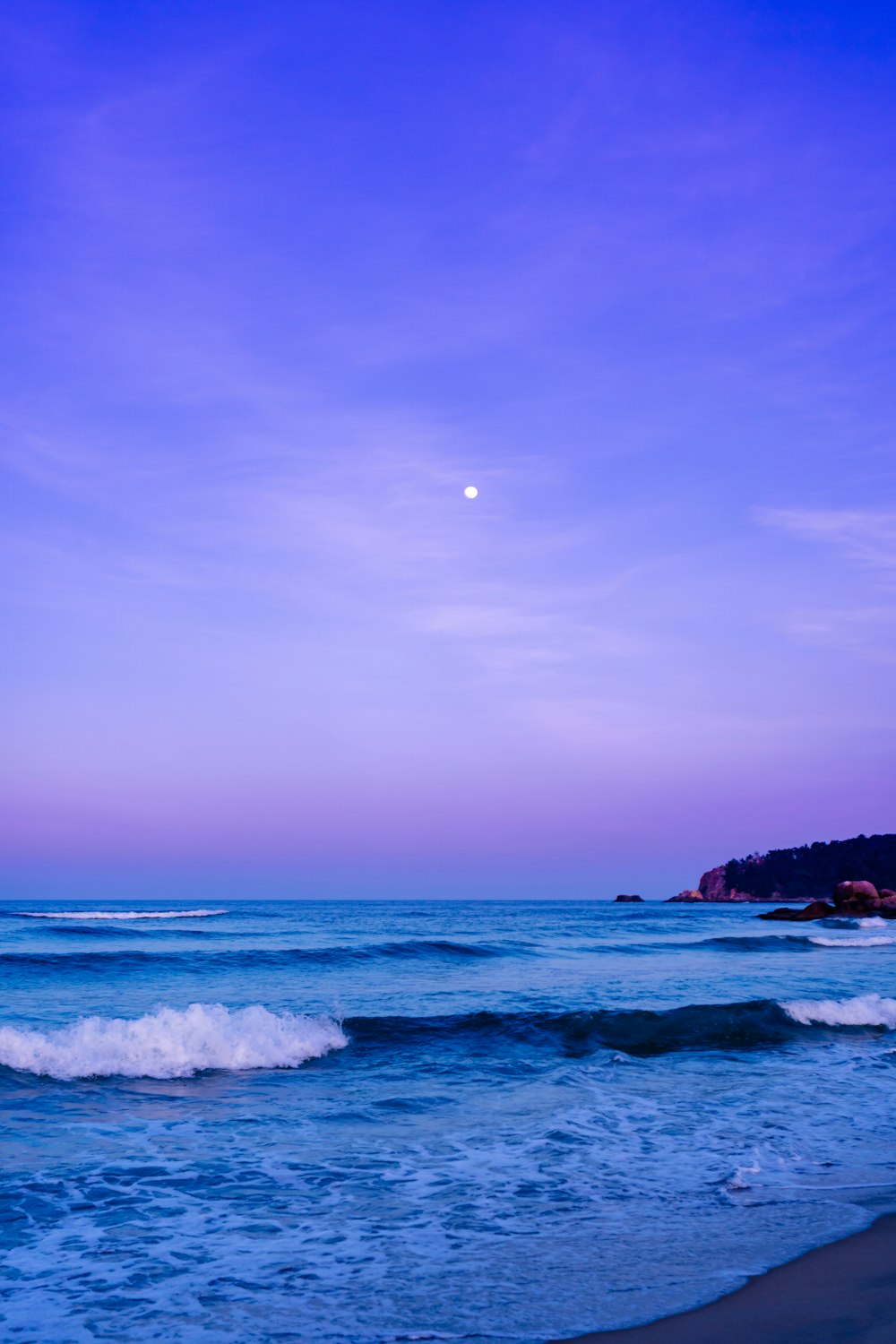 a beach with waves and a full moon in the sky