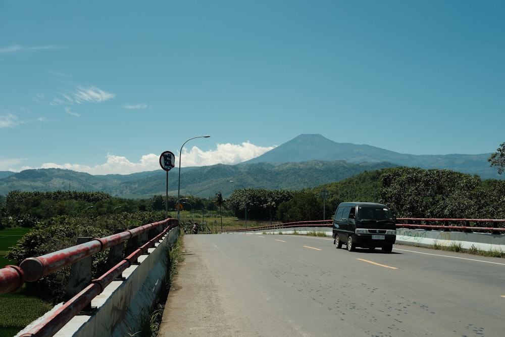 a black truck driving down a road next to a lush green hillside