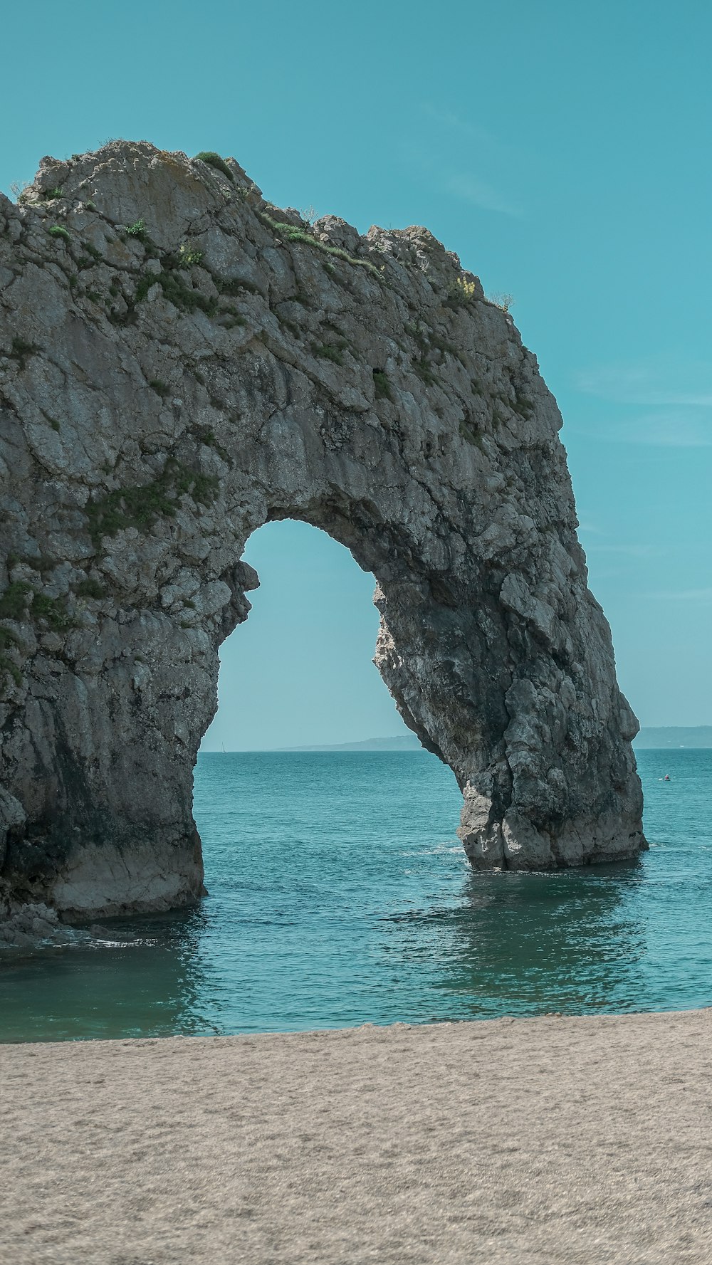 a large rock formation in the ocean near a beach