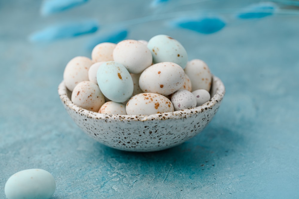 a bowl of speckled eggs on a blue surface