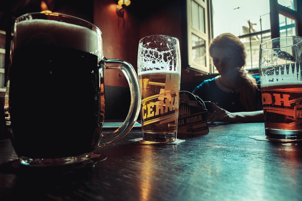 a woman sitting at a table with two mugs of beer