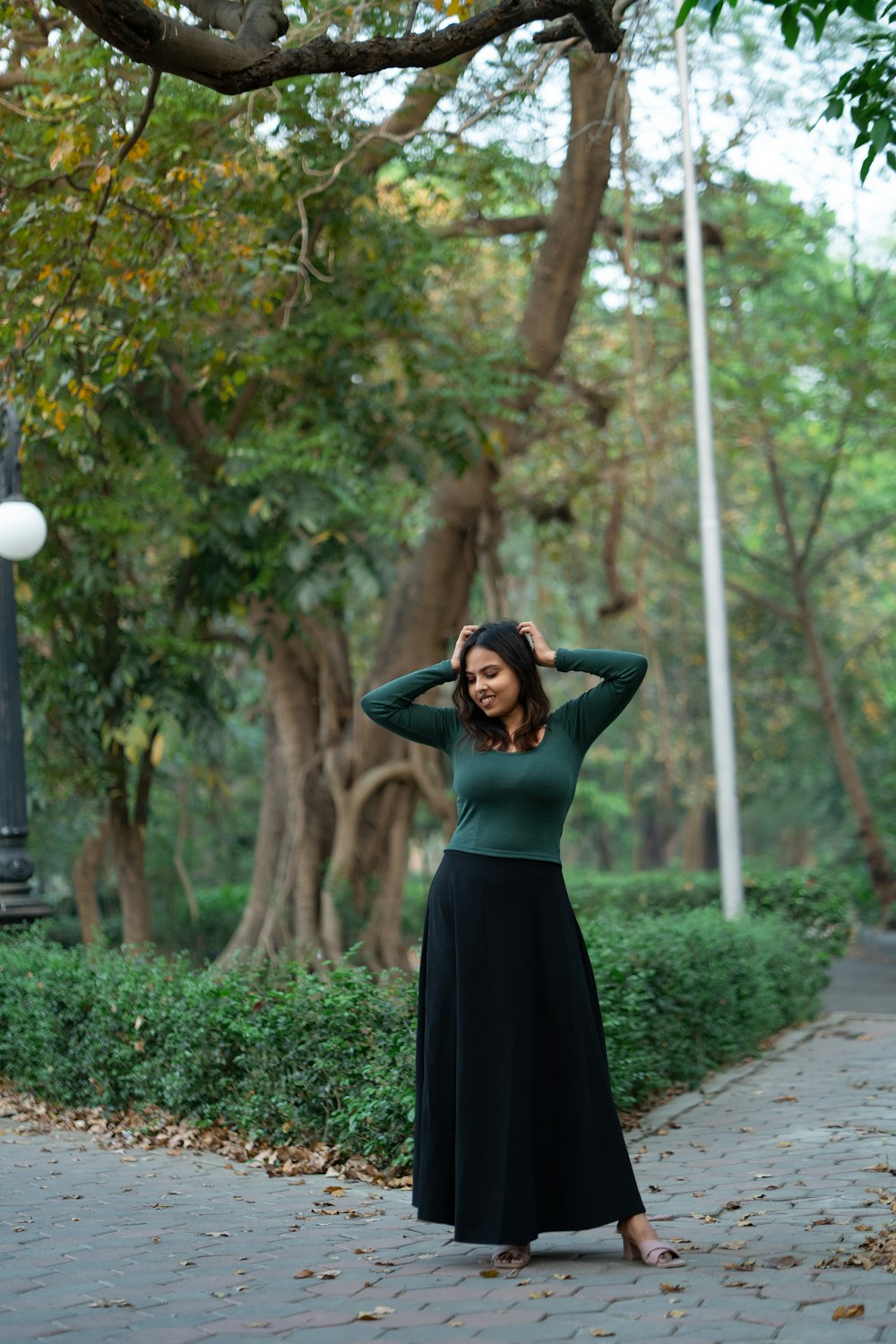 a woman standing on a sidewalk in a green shirt and black skirt